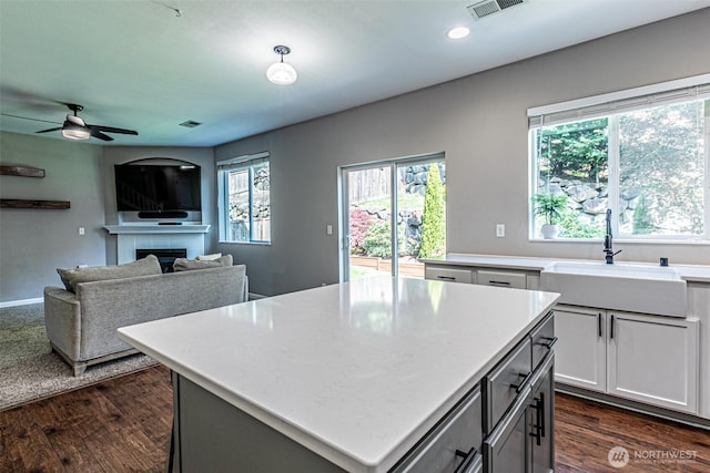 kitchen featuring ceiling fan, visible vents, a tile fireplace, a sink, and light countertops