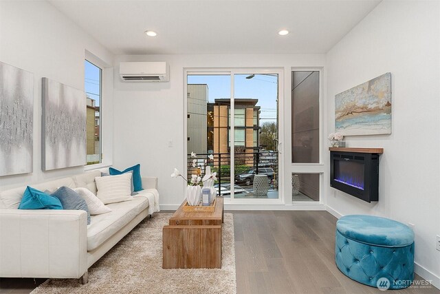 living area featuring a wall unit AC, wood finished floors, healthy amount of natural light, baseboards, and recessed lighting