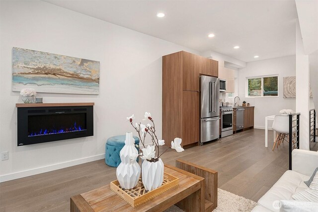 living area with wood finished floors, baseboards, recessed lighting, and a glass covered fireplace