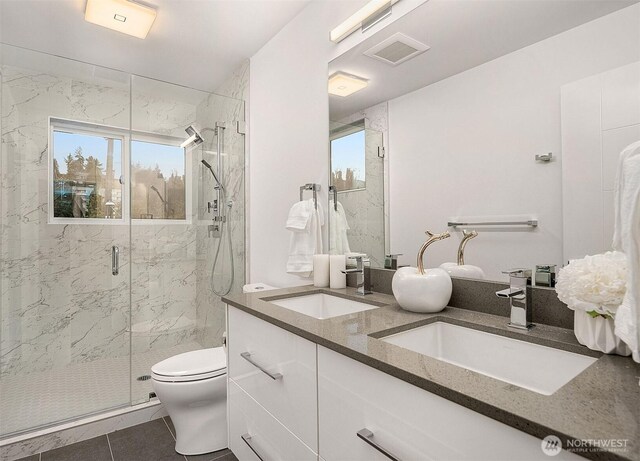 bathroom featuring a marble finish shower, toilet, double vanity, and tile patterned floors