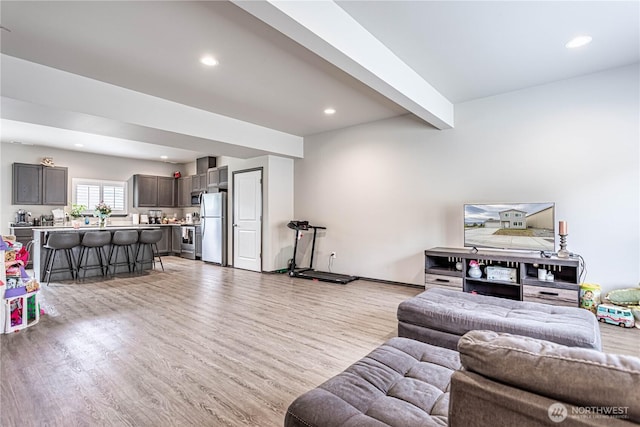 living room featuring baseboards, beam ceiling, recessed lighting, and light wood-style flooring