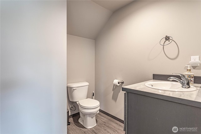half bath with vaulted ceiling, wood finished floors, vanity, baseboards, and toilet