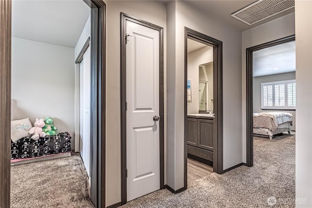 hall featuring baseboards, light colored carpet, a sink, and visible vents