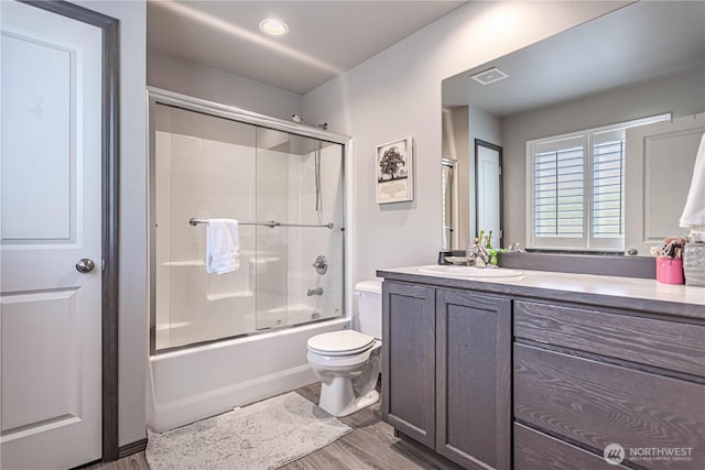 bathroom featuring vanity, toilet, wood finished floors, visible vents, and bath / shower combo with glass door