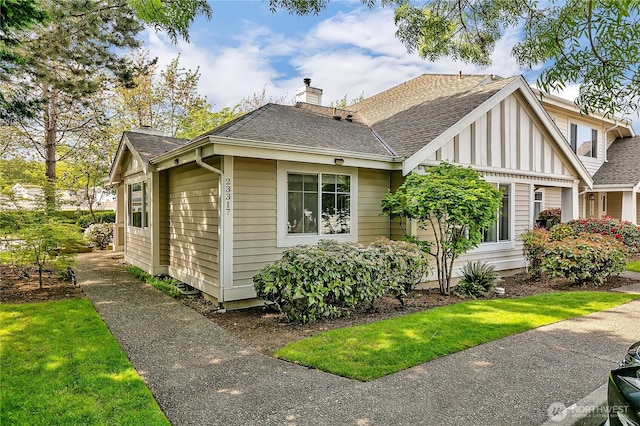 view of front of home with a shingled roof, a chimney, and a front lawn