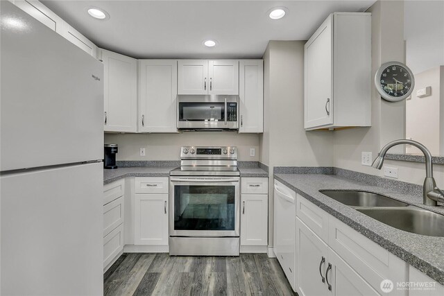 kitchen with white cabinets, appliances with stainless steel finishes, a sink, recessed lighting, and dark wood-type flooring
