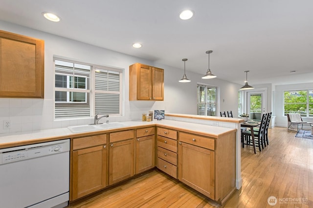 kitchen with decorative light fixtures, white dishwasher, a sink, a peninsula, and light wood-style flooring