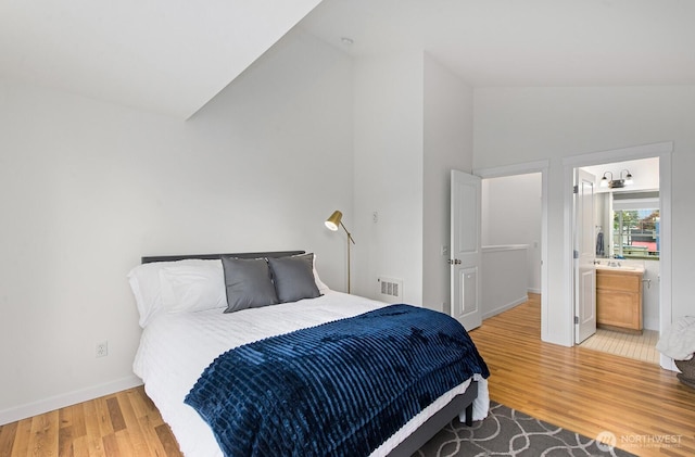 bedroom featuring visible vents, light wood-type flooring, baseboards, connected bathroom, and lofted ceiling