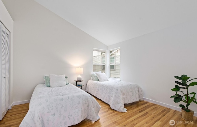 bedroom with a closet, baseboards, vaulted ceiling, and light wood-type flooring