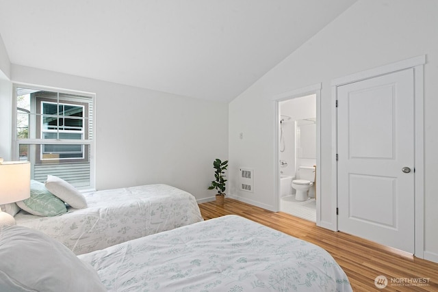 bedroom featuring heating unit, wood finished floors, lofted ceiling, baseboards, and connected bathroom