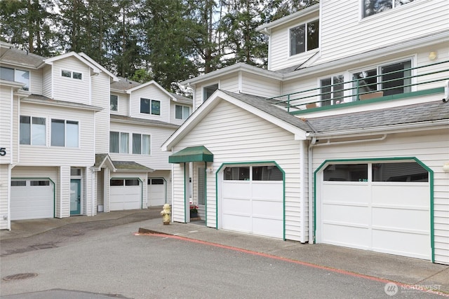 exterior space featuring an attached garage, a shingled roof, and a balcony
