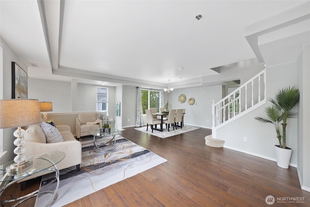 living room with visible vents, stairs, wood finished floors, a tray ceiling, and a notable chandelier