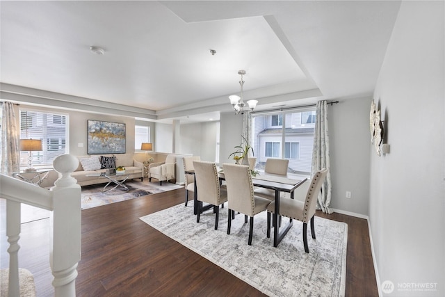 dining space featuring baseboards, a tray ceiling, a notable chandelier, and dark wood finished floors