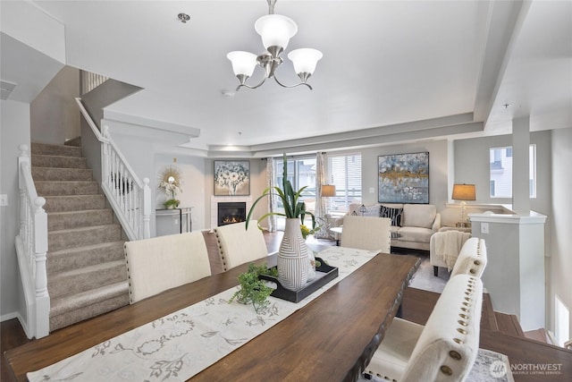 dining area featuring an inviting chandelier, a glass covered fireplace, wood finished floors, and stairway