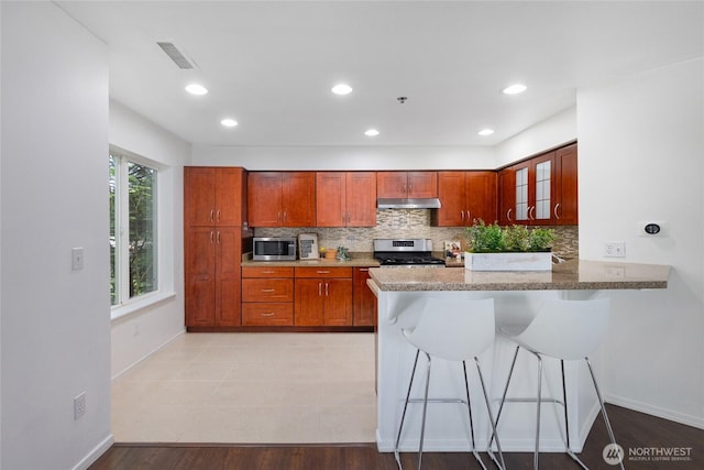 kitchen with visible vents, a kitchen breakfast bar, under cabinet range hood, appliances with stainless steel finishes, and backsplash