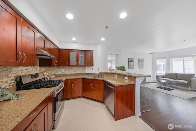 kitchen with appliances with stainless steel finishes, a sink, a peninsula, open floor plan, and under cabinet range hood