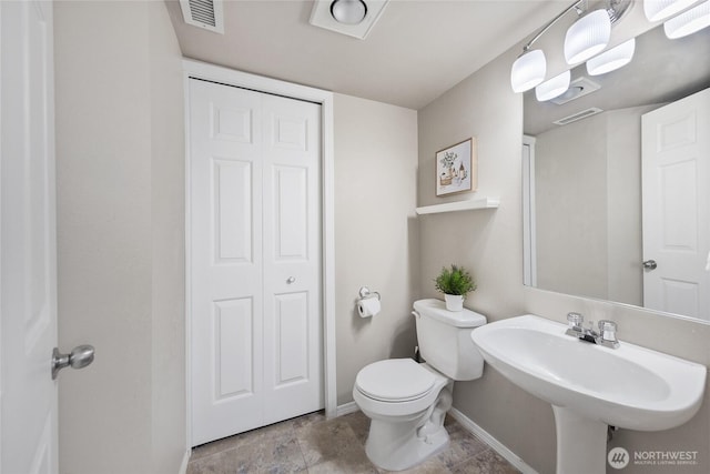 half bathroom with toilet, baseboards, visible vents, and a sink