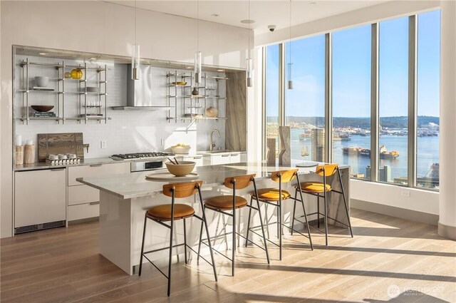 2510 6th Ave Unit 602, Seattle, WA 98121 - kitchen featuring wall chimney exhaust hood, modern cabinets, light wood-style floors, white cabinetry, and a breakfast bar area
