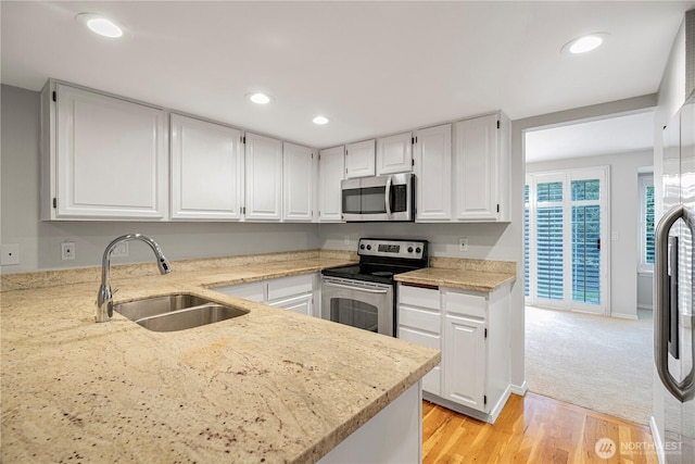 kitchen with stainless steel appliances, a sink, light stone counters, white cabinets, and recessed lighting