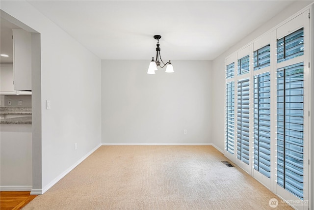 empty room with baseboards, light colored carpet, and a chandelier