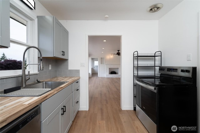 5310 Sunset Ave, Anacortes, WA 98221 - kitchen featuring appliances with stainless steel finishes, butcher block counters, light wood-type flooring, a fireplace, and decorative backsplash