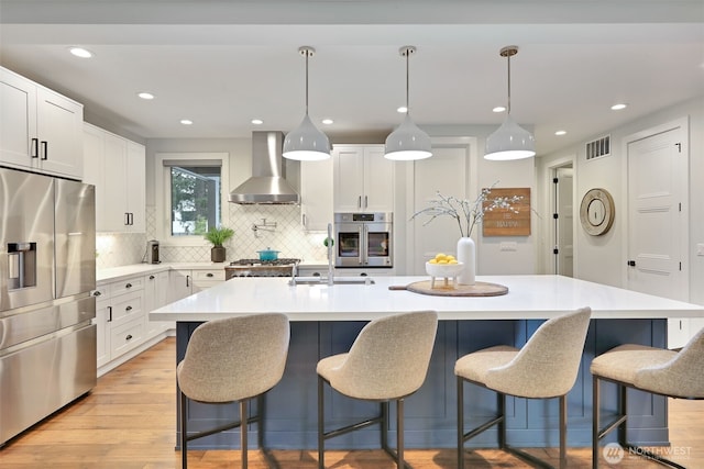 kitchen with visible vents, wall chimney range hood, light countertops, tasteful backsplash, and appliances with stainless steel finishes