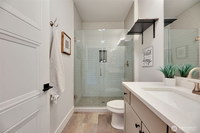 bathroom featuring toilet, wood finished floors, vanity, a stall shower, and baseboards