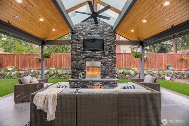 view of patio / terrace with a fenced backyard, an outdoor living space with a fireplace, and a ceiling fan