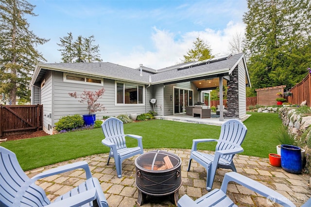 rear view of property with a patio area, a yard, a fenced backyard, roof mounted solar panels, and an outdoor living space with a fire pit