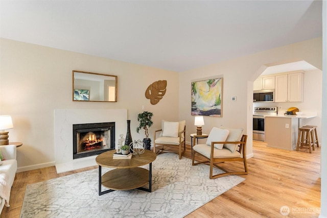 living room featuring a fireplace, arched walkways, baseboards, and light wood-type flooring