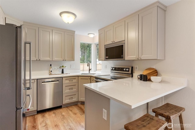 kitchen with a peninsula, a kitchen breakfast bar, light wood-type flooring, a sink, and stainless steel appliances