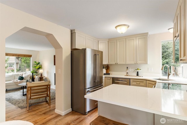 kitchen with light countertops, appliances with stainless steel finishes, a sink, and light wood-style floors