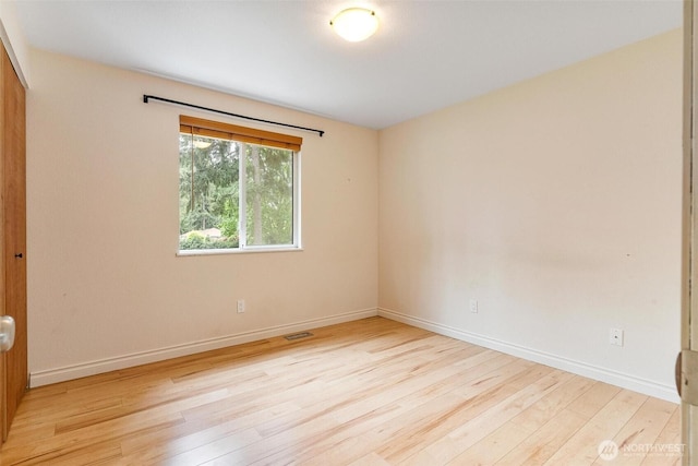 unfurnished room featuring baseboards, visible vents, and wood finished floors