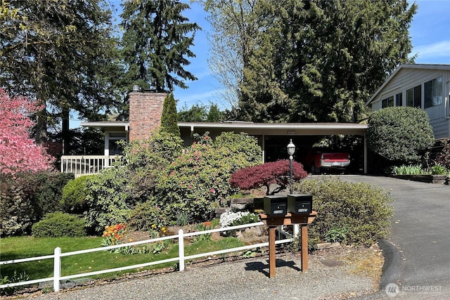 view of front of property featuring fence, driveway, a chimney, and a carport