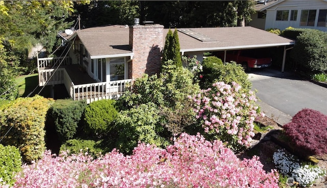 view of front facade with aphalt driveway, a chimney, stairs, a shingled roof, and a carport