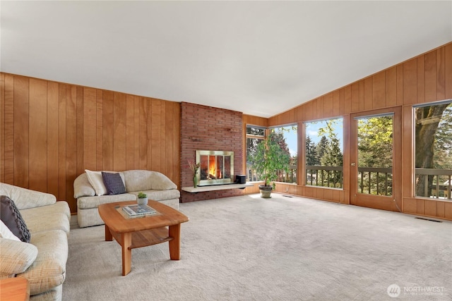 living area with wooden walls, vaulted ceiling, carpet floors, and a fireplace