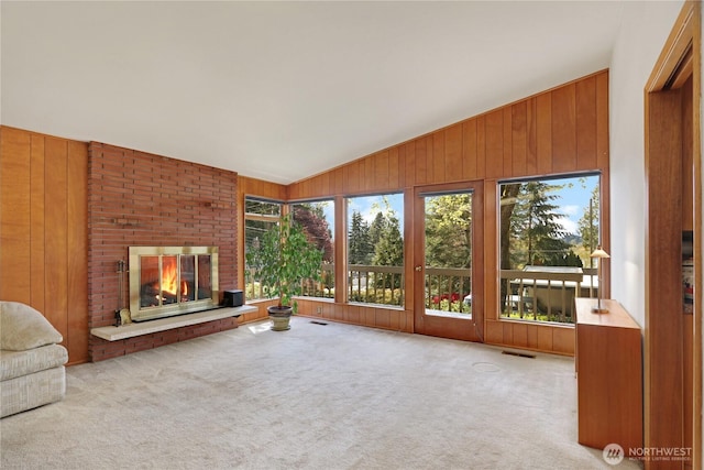 unfurnished living room with carpet flooring, wooden walls, vaulted ceiling, and a brick fireplace