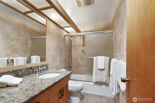 full bath featuring visible vents, vanity, toilet, tile walls, and enclosed tub / shower combo