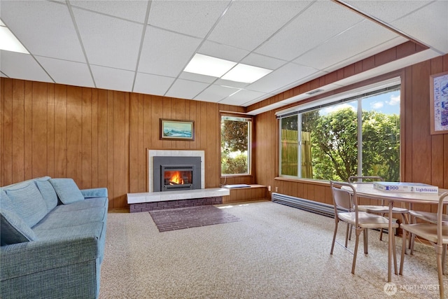 carpeted living room featuring baseboard heating, wood walls, a paneled ceiling, and a fireplace