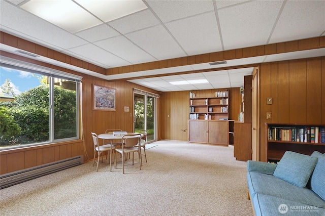 sitting room with carpet floors, a baseboard heating unit, wood walls, and visible vents