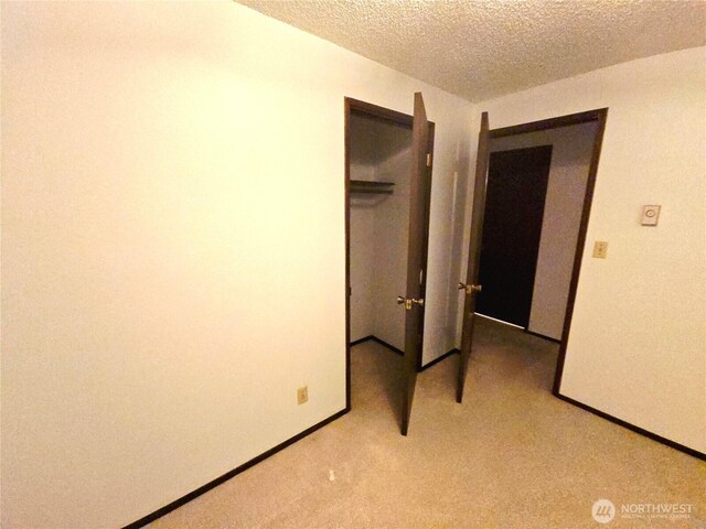 unfurnished bedroom with light colored carpet, a textured ceiling, baseboards, and a closet