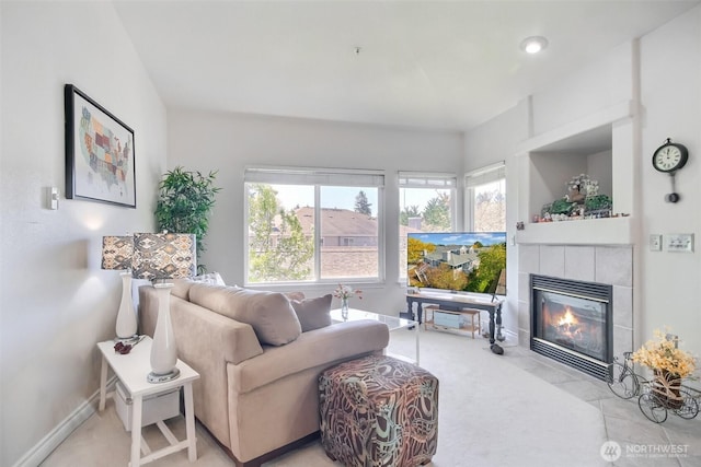 living area featuring baseboards, light colored carpet, a tiled fireplace, and a wealth of natural light