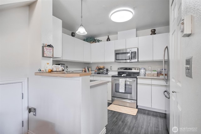 kitchen featuring wood finished floors, light countertops, white cabinets, appliances with stainless steel finishes, and decorative light fixtures