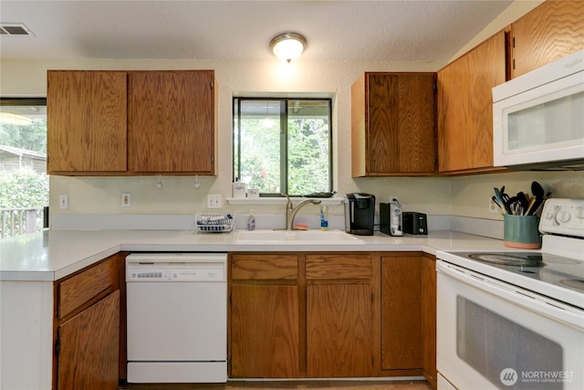 kitchen with white appliances, a sink, light countertops, and brown cabinetry