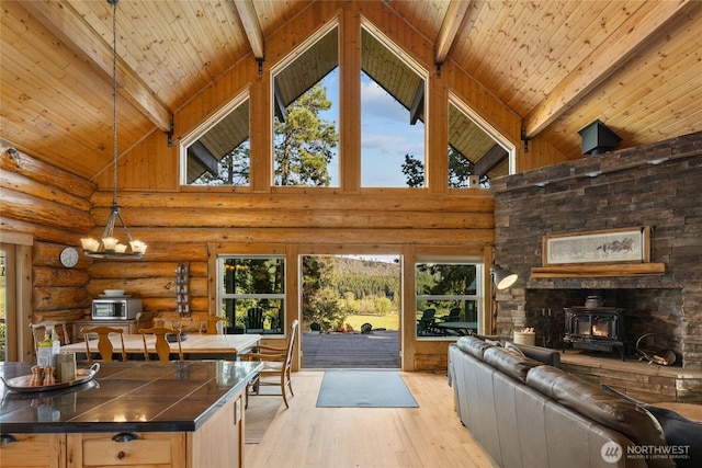 living area with high vaulted ceiling, light wood finished floors, a wood stove, beam ceiling, and healthy amount of natural light