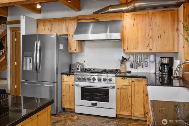 kitchen featuring stainless steel appliances, wall chimney range hood, a sink, and dark stone finish floors