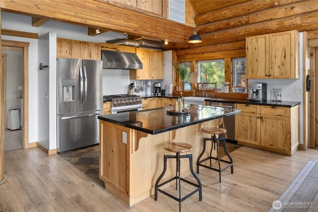 kitchen featuring stainless steel appliances, wall chimney range hood, a sink, light wood finished floors, and dark countertops