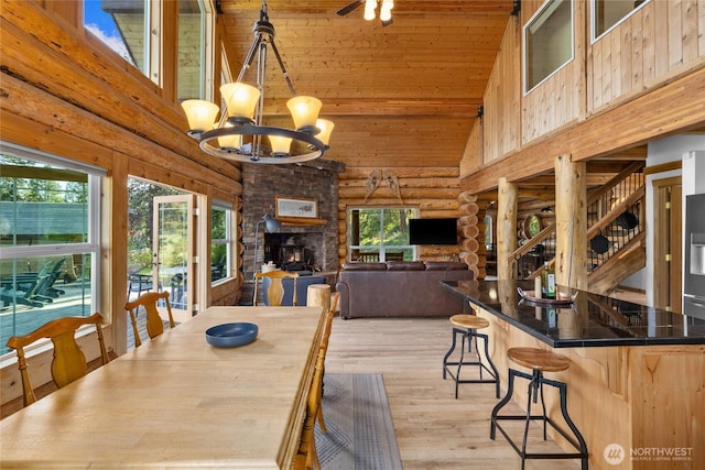 dining space featuring rustic walls, a chandelier, high vaulted ceiling, light wood-type flooring, and healthy amount of natural light