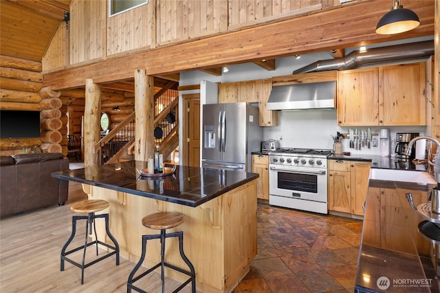 kitchen with gas range oven, stainless steel fridge, rustic walls, a sink, and wall chimney range hood