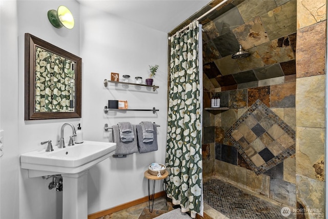 full bath with tiled shower, baseboards, and stone finish flooring